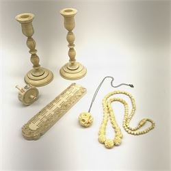 A group of ivory, comprising a pair of candlesticks with turned stems, H14.5cm, a cribbage board with carved border depicting dragons, a carved puzzle ball pendant, and carved necklace, the beads carved as flowers, plus a bone spinning top. 