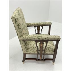 Late 19th century Arts and Crafts mahogany armchair, upholstered in a pale ground fabric decorated with trailing foliage and flower heads, pierced splats to each side with stylised flower inlay, square tapering supports, brass castors