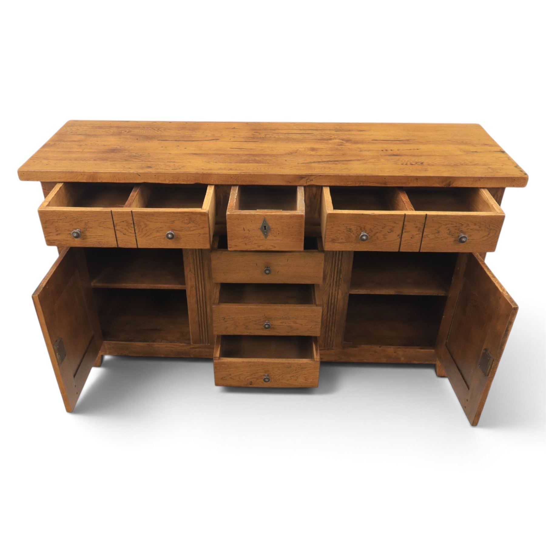 Indigo Furniture - large rustic oak sideboard fitted, with three drawers above three central drawers, flanked by fielded panelled doors, raised on bracket feet