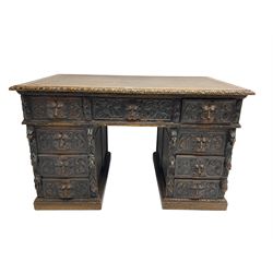 Late 19th century Gothic revival carved oak twin pedestal desk, rectangular top with inset writing surface and carved edges, central frieze drawer flanked by eight drawers, all with green man carved handles and extending trailing foliage, carvings of pineapple and lion mask corbels, the pedestals with panelled sides and back, on plinth bases