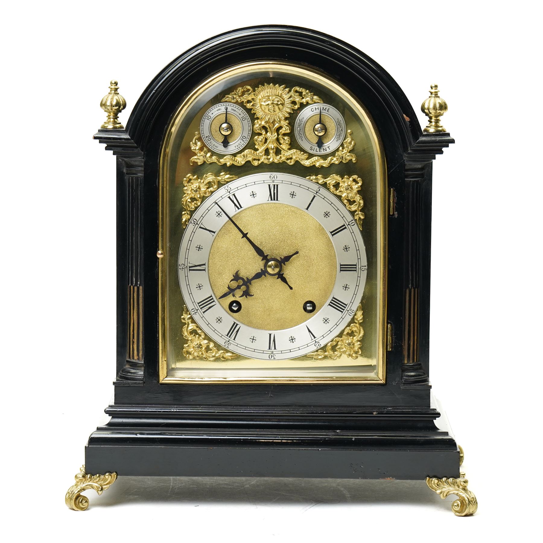 Winterhalder & Hoffmeier-8-day early 20th century mantel clock with an ebonised finish, break arch pediment and two matching brass finials, conforming glazed door with a cast brass bezel flanked by reeded quarter pilasters, on a moulded plinth with scroll feet, brass dial with cast spandrels and strike/silent and pendulum regulation dials to the arch, matted dial centre with a silvered chapter, Roman numerals  and gothic steel hands, dial pinned to a quarter striking movement sounding the quarters on two gongs and hours on one. With Pendulum.
