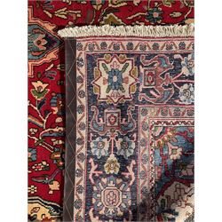 Central Persian Isfahan crimson ground carpet, central floral medallion in ivory and blue, set within a field of dense floral patterns, bordered by a navy band decorated with stylised flower heads and vines