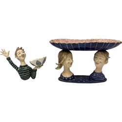 Ceramic 'girl and boy dish', by Helen Kemp, an oval dish with a mottled pink ground and gilt edging upon the sculpted heads of a girl and a boy, together with a 'boy sconce', by Helen Kemp, a sculpted boy holding a small bowl with foliate decoration, both with the artist's mark beneath.