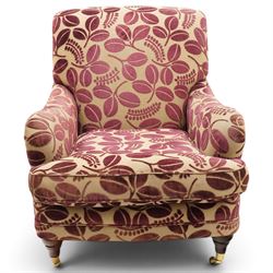Traditional Howard shape armchair, rolled back and arms over deep seat, raised on turned supports with brass cups and castors, upholstered in plum foliate patterned fabric with loose seat cushion