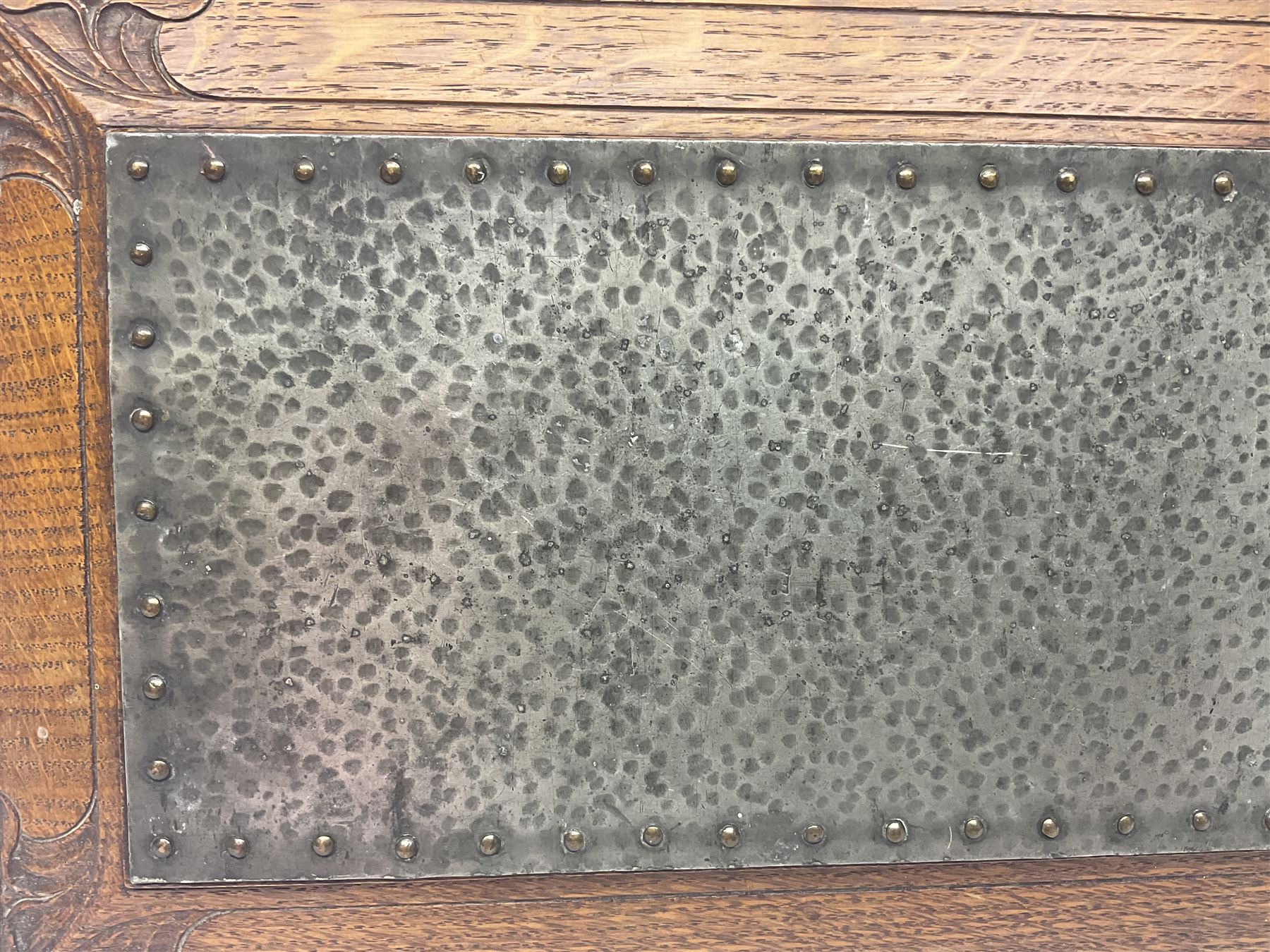 Arts and Crafts oak stand by Arthur Simpson of Kendal, of rectangular form with central hammered pewter panel, surrounded by a border with carved foliate corners, upon two bar supports, bearing label detailed 