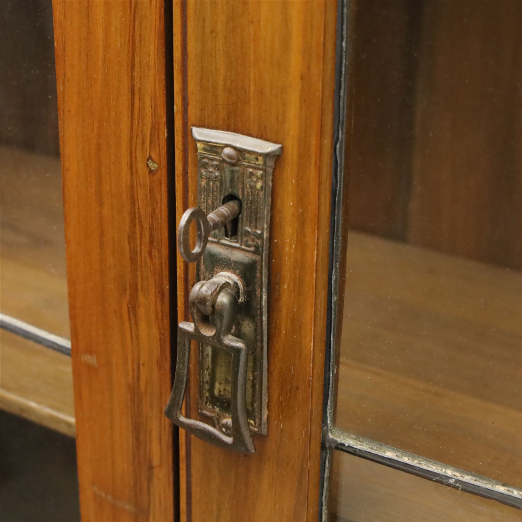 20th century wooden bookcase cabinet, fitted with a pair of leaded glass panel doors opening to adjustable shelves, the base top and front veneered in richly figured walnut, contrasted with solid oak panelled sides and shaped lower frieze, terminating in castors