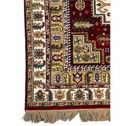 Indian woollen crimson ground rug, the field decorated with three stepped medallions surrounded by stylised plant motifs, the borders with repeating leaf design 