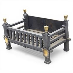 Arts and Crafts cast iron fire grate, rectangular backplate with plain upper rail over a slatted front of cylindrical tapering bars, flanked by square section uprights with fluted detail and scroll terminals, raised on stepped feet with shaped brass roundel mounts and brass finials to the corner posts