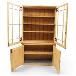 19th century pine glazed bookcase cupboard, twin astragal glazed doors with stained glass corner panels, enclosing fixed shelves, the lower section fitted with two panelled cupboard doors enclosing single shelf, on plinth base