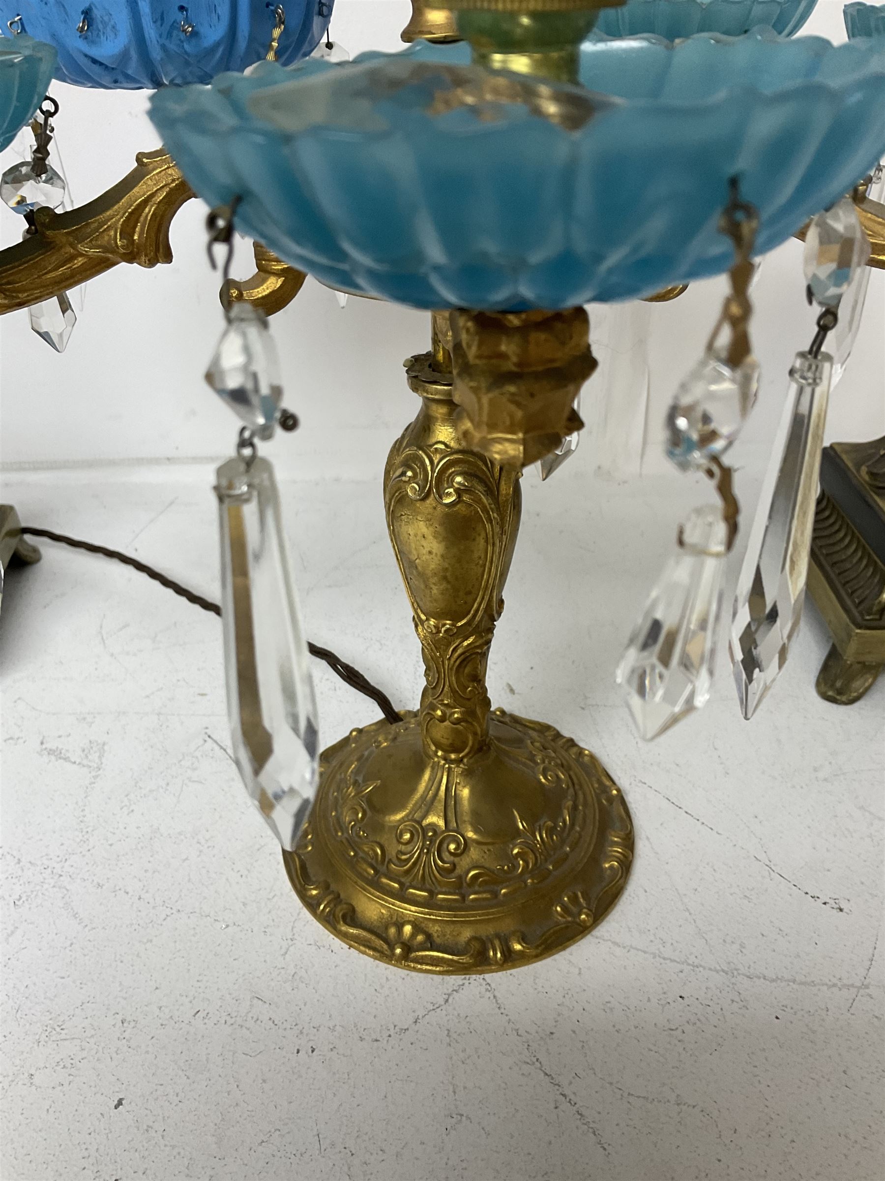 Brass table lamp, modelled as a candelabra with five branches, each with blue glass candle holders with crystal drops, H47cm, together with a pair of cast metal table lamps with acanthus leaf detail, upon a stepped square base, with red fabric feather and tassel shades, H78cm