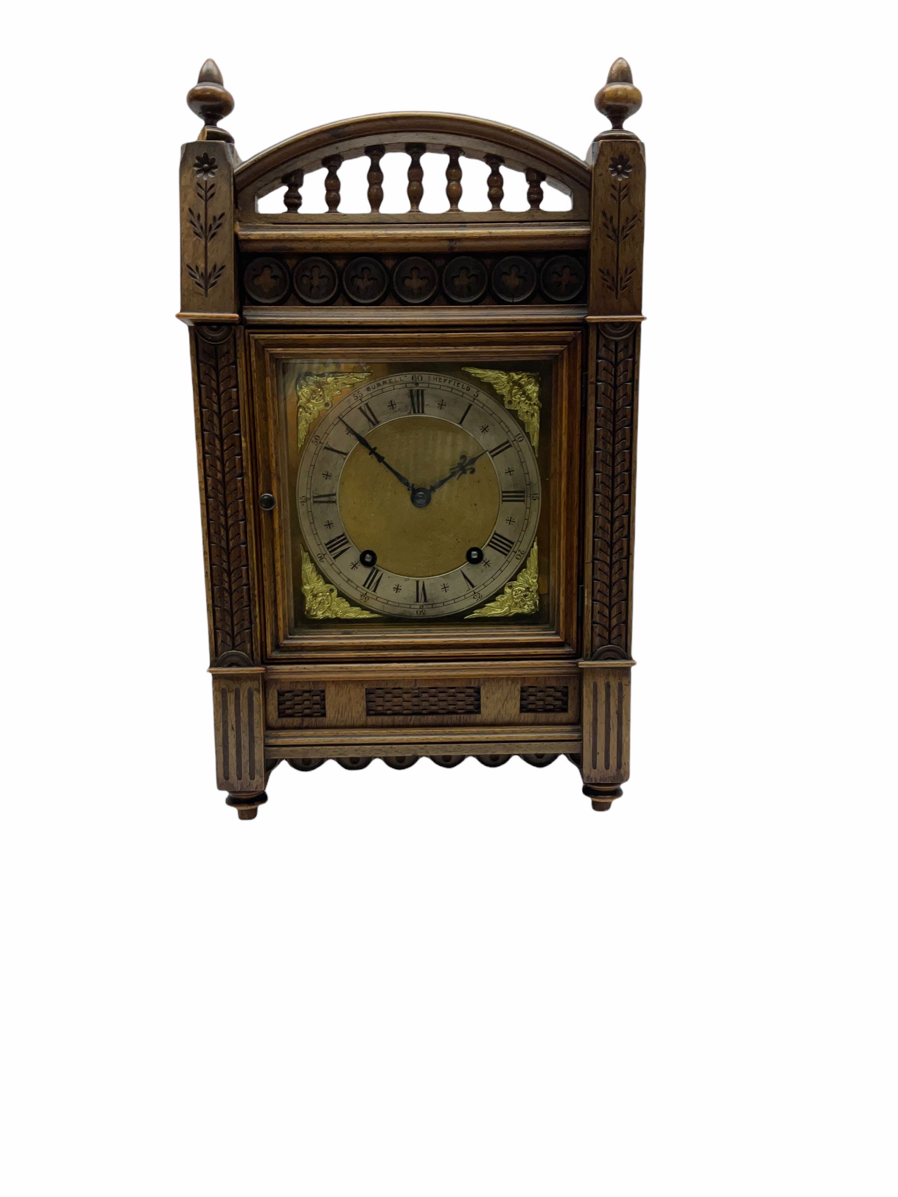 A late 19th century Winterhalder & Hofmeier quarter striking eight-day mantle clock striking the hours and quarters on two coiled gongs, with a recoil escapement and double quarter rack strike, in an aesthetic movement oak case with incised carving, trefoil frieze, raised turned finials and baluster pediment, case door with sound fret, square brass dial, silvered chapter ring with roman numerals, minute track and half hour markers, steel Fleur de Lys hands and cherub face spandrels, dial inscribed “Burrell Sheffield”.
With pendulum & Key.
