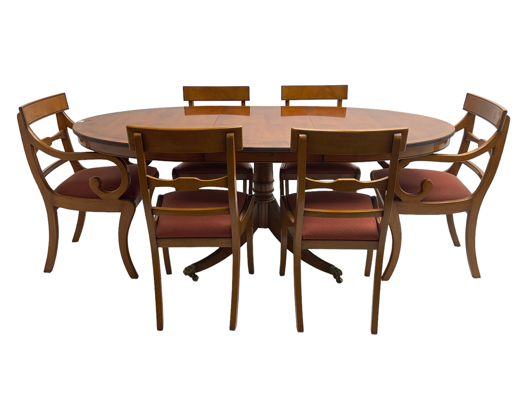 Regency design yew wood dining table, oval cross-banded top with reeded edge, raised on turned pedestal with reeded sabre supports terminating in brass hairy paw feet and castors (W138cm D100cm H75cm); and Rackstraw - set six (4+2) Regency design dining chairs with red drop-in seats (W50cm H86cm)