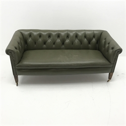Low back settee upholstered in buttoned green leather, square tapering supports with brass cups and castors, W155cm
