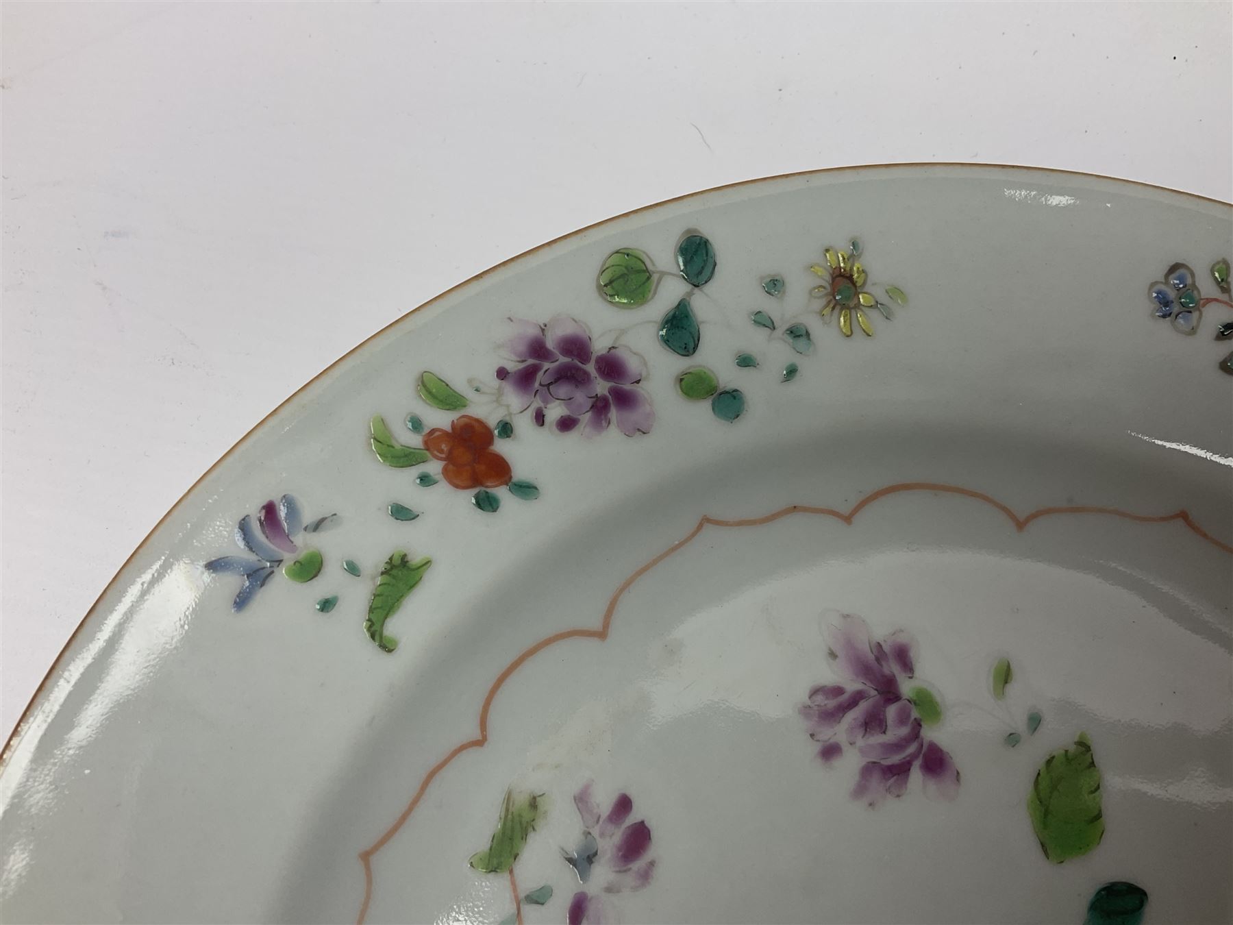 Three 18th century Chinese Famille Rose plates, the first example enamelled with blossoming peonies, rockwork and fence, the other two examples of similar design, decorated with blossoming peonies and sprigs within shaped inner borders, each approximately D23cm