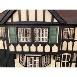Large Tri-ang No.93 doll`s house in the 'Stockbroker's Range' c1935; two-storey double-fronted Tudor design, half timbered gables, two-storey bay windows, cream and mock shrubbery to front, opening metal framed windows with green shutters, red simulated tiled roof with chimney, integral garage with opening doors, front elevation has four hinged doors opening to reveal two bedrooms with fire places, living room, bathroom and kitchen with built in dresser and sink, entrance hall and staircase, side entrance with porch and seat and sun dial over on chimney stack; some wiring for electrical lighting; metal Tri-ang Toys disc verso; comprehensively furnished H66cm L117cm D43cm