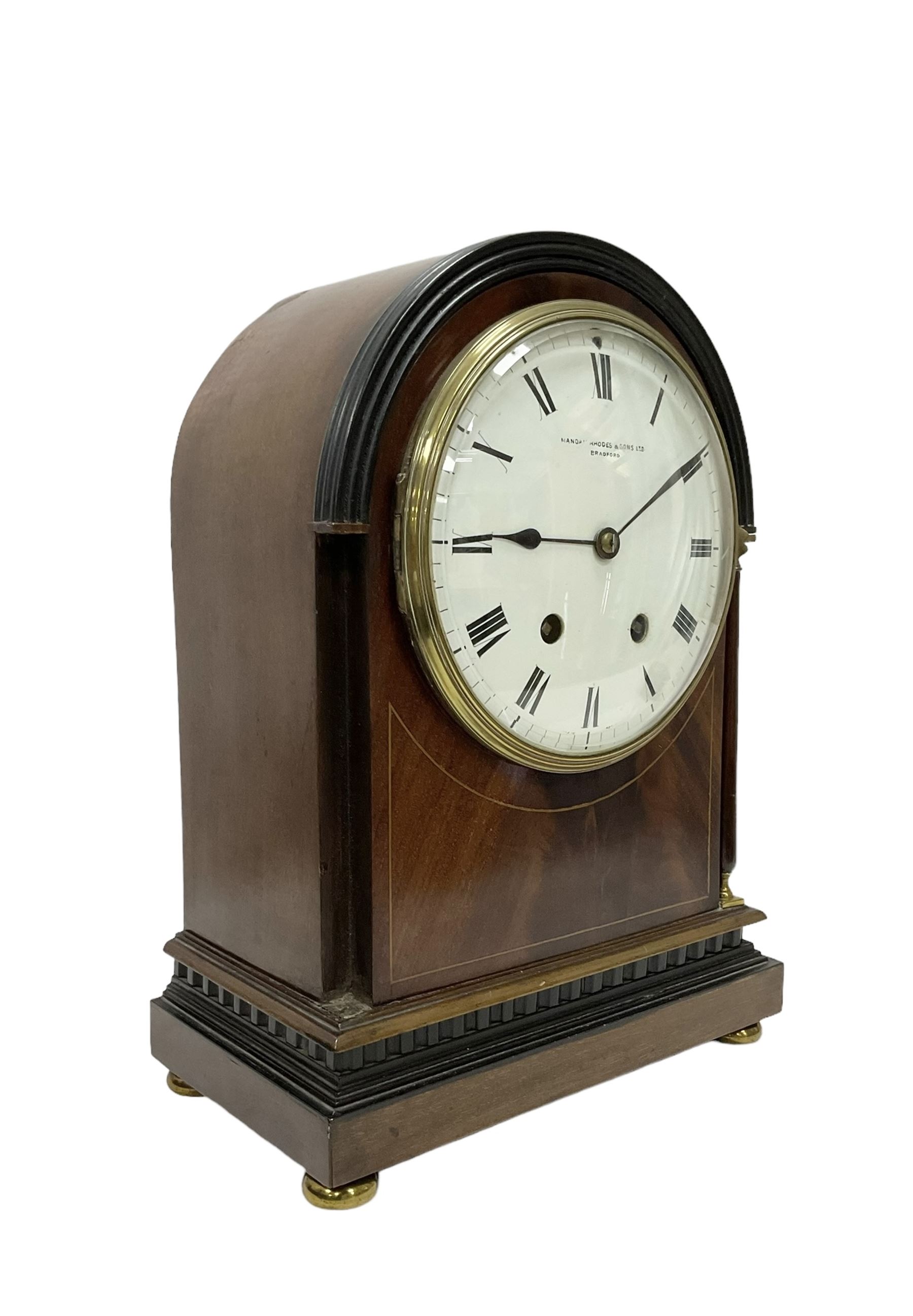 Manoah Rhodes & Son of Bradford, - Edwardian mahogany domed top mantle clock with a French 8-day movement striking the hours and half hours on coiled gong, case with inlaid stringing and raised on brass button feet, convex enamel dial with Roman numerals and steel spade hands. With pendulum and key.