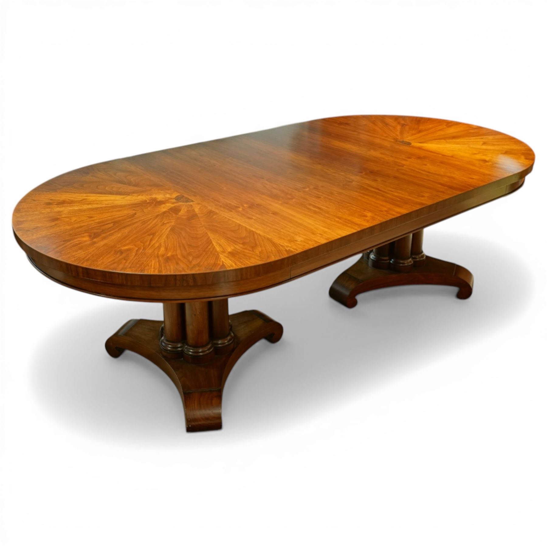 Late 20th century Regency design walnut twin pedestal dining table, the oval top with radial sunburst veneered ends centred by roundels, upon twin pedestal turned column supports, issuing to down swept triform bases