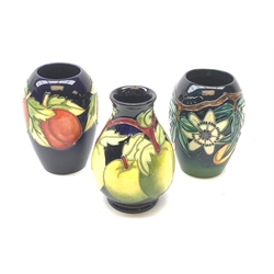 Three Moorcroft vases, the first of bulbous form tube line decorated with green apples against a dark blue glazed ground, the other examples of ovoid form, the first tube line decorated with plums against a dark blue glazed ground, the second decorated in the Passion Fruit pattern, each with marks beneath, tallest H14cm. 