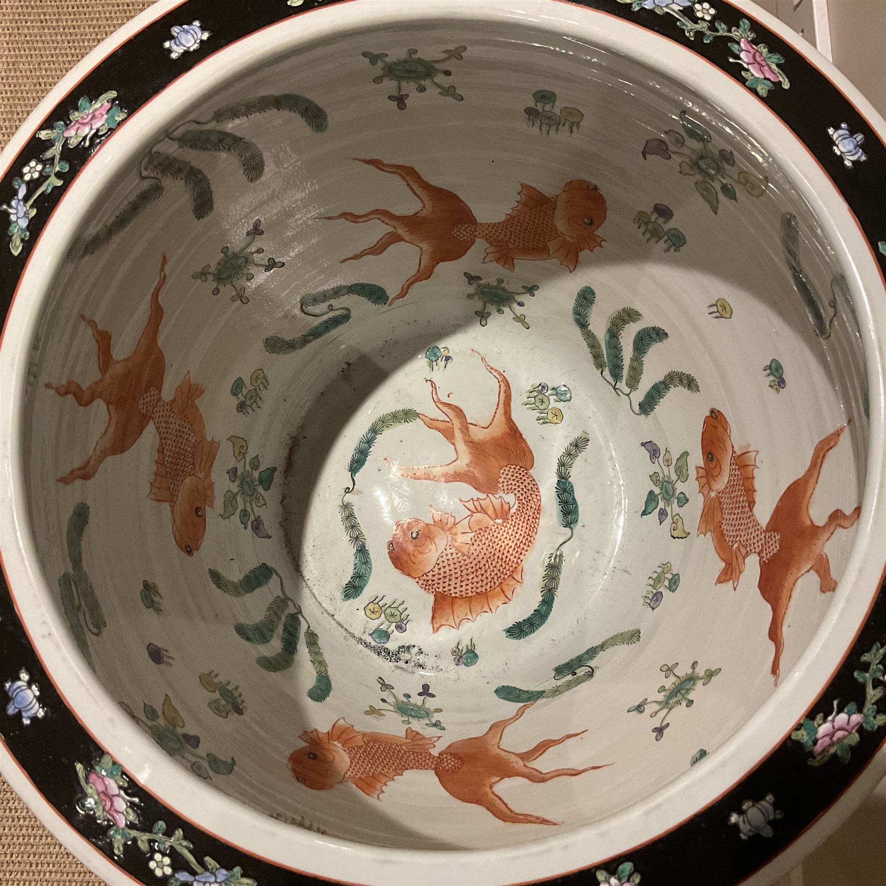 Large 20th century Chinese famille noir glazed porcelain jardinière, of ovoid form, the exterior enamelled with butterflies and white cranes amidst blossoming water lilies and pads against a black ground, between two stylised polychrome borders and beneath a key border to rim, the interior enamelled with red koi fish swimming amongst water fronds and weeds, with printed red character mark beneath, the whole upon an ebonised hardwood stand with three cabriole legs, jardinière H42cm D47cm, including stand overall H69.5cm