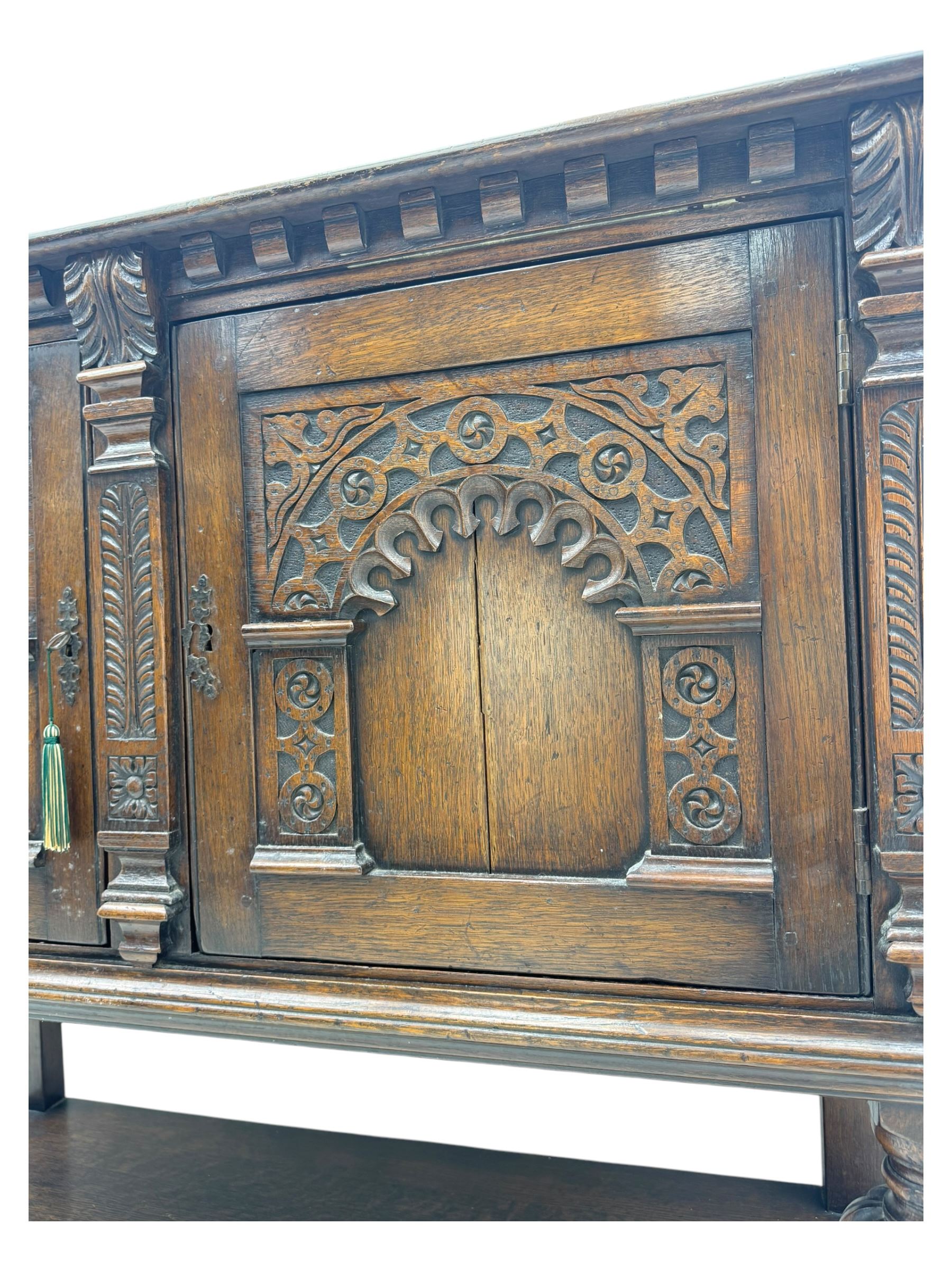 Jacobean design carved oak two door cupboard, the frieze and twin cupboard doors carved with arcaded panels and stylised foliage, raised on baluster supports united by an undertier