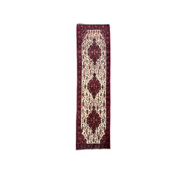 North West Persian Saveh crimson ground runner rug, the three lozenge pole medallions in an ivory field, surrounded by stylised plant motifs, the guarded border decorated with repeating geometric patterns