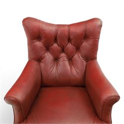 Early 20th century style oxblood red leather Chesterfield armchair, deep buttoned shaped back over padded scroll arms and loose seat cushion, raised on turned mahogany front supports with brass caps and castors