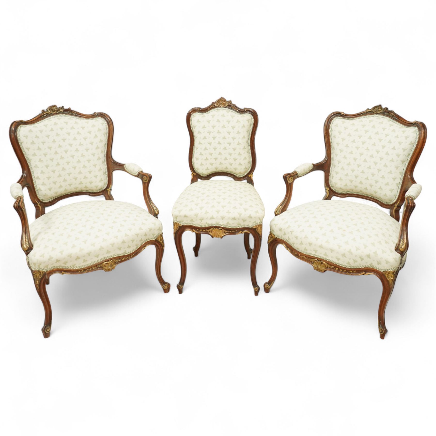 Louis XV design salon suite comprising a pair of walnut and parcel-gilt fauteuil armchairs together with a side chair, the cresting rail surmounted with a carved giltwood floral shell motif with extending foliage, the cartouche shaped backs and sprung seats upholstered in pale blue patterned fabric, over a shaped apron with scallop decoration and foliage carved knees, raised on cabriole supports