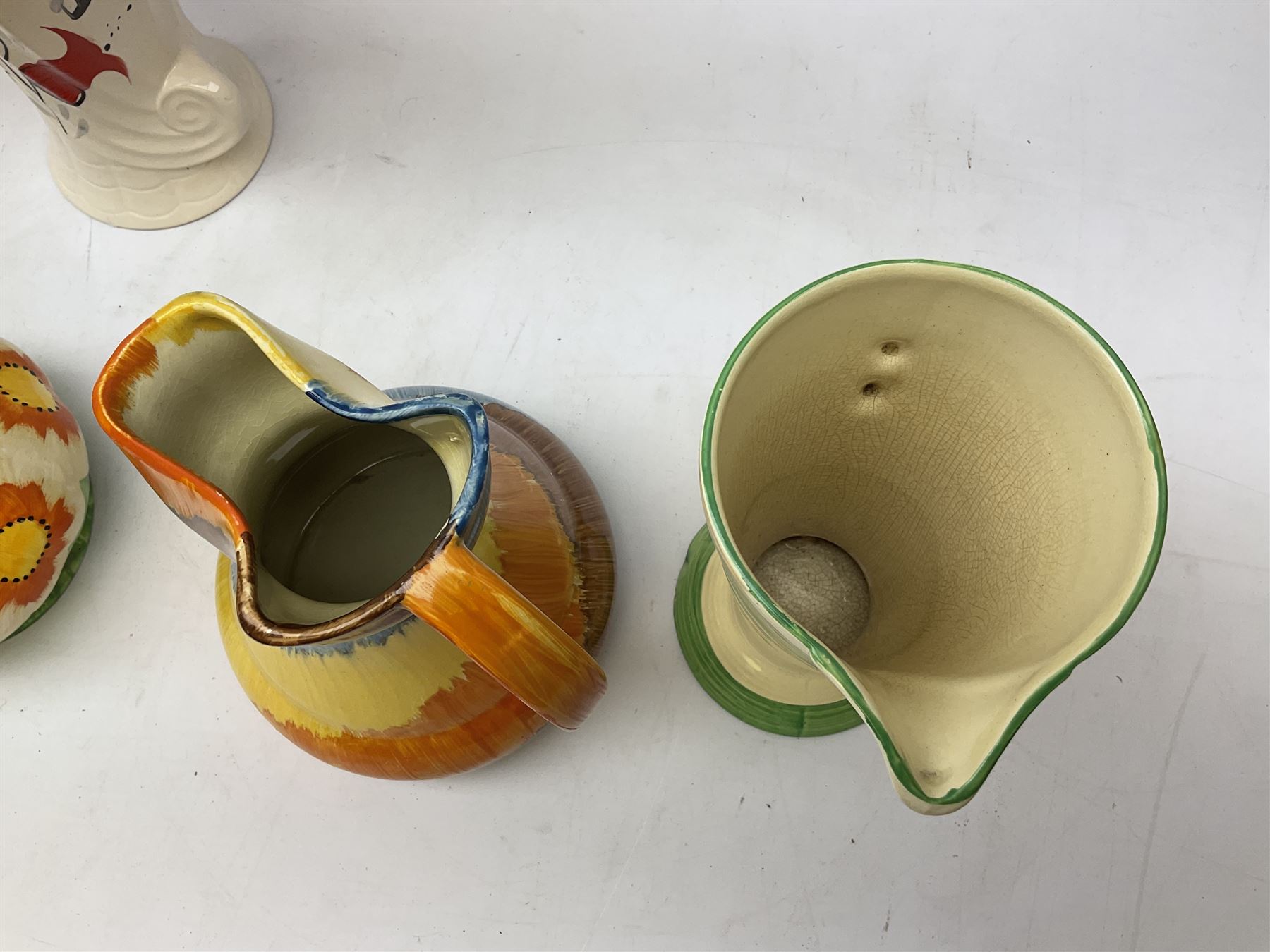 Group of Art Deco ceramics, comprising Wadeheath jug painted in spiralled bands of blue, orange, yellow and brown, shape no. 707784, Royal Doulton Caprice pattern twin handled bowl, no. D5358, Arthur Wood wall pocket of typical stylised fan form with painted floral decoration, Arthur Wood vase of cornucopia form with red and grey floral decoration, Wadeheath jug of ribbed form with stylised handle, and two Hancock's Ivory Ware jugs, tallest example H26cm