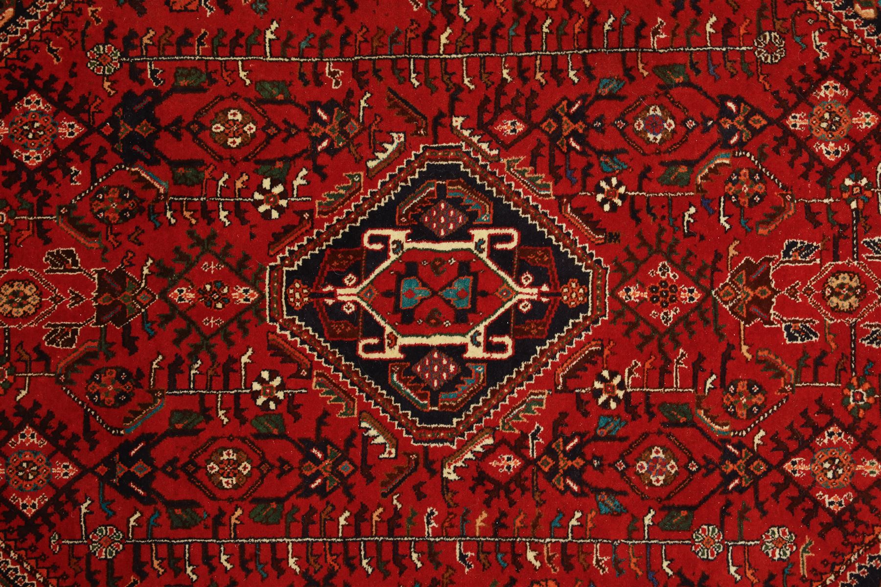 Persian tribal hand-knotted rug, crimson ground, madder field with central stepped lozenge medallion with scattered floral and geometric spandrels with rosette border 
