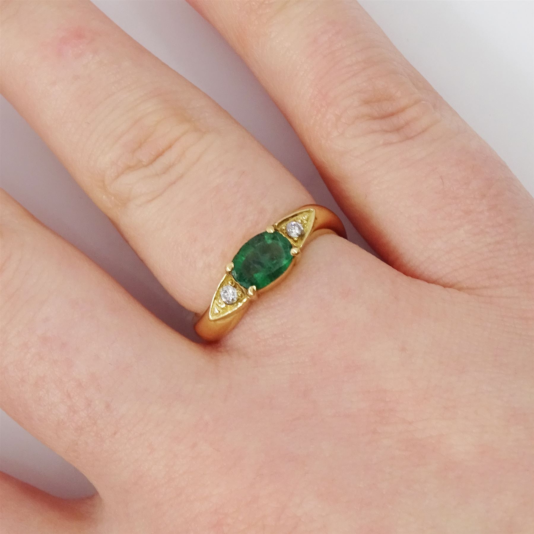 14ct gold emerald and diamond three stone ring, oval cut emerald with a round brilliant cut diamond set either side, to a wave design shank