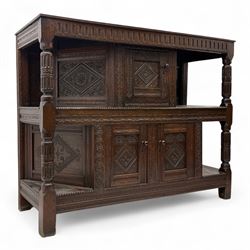 Early 20th-century  oak Jacobean two-tier revival court cupboard, rectangular top with carved notch and stylized foliate carved edge above a carved lozenge pattern frieze and a central cupboard with carved geometric designs and geometric carved panelled sides, above a carved panelled cupboard with two doors of similar geometric design, the whole flanked by two sets of stop-fluted baluster turned columns and supported on stile feet