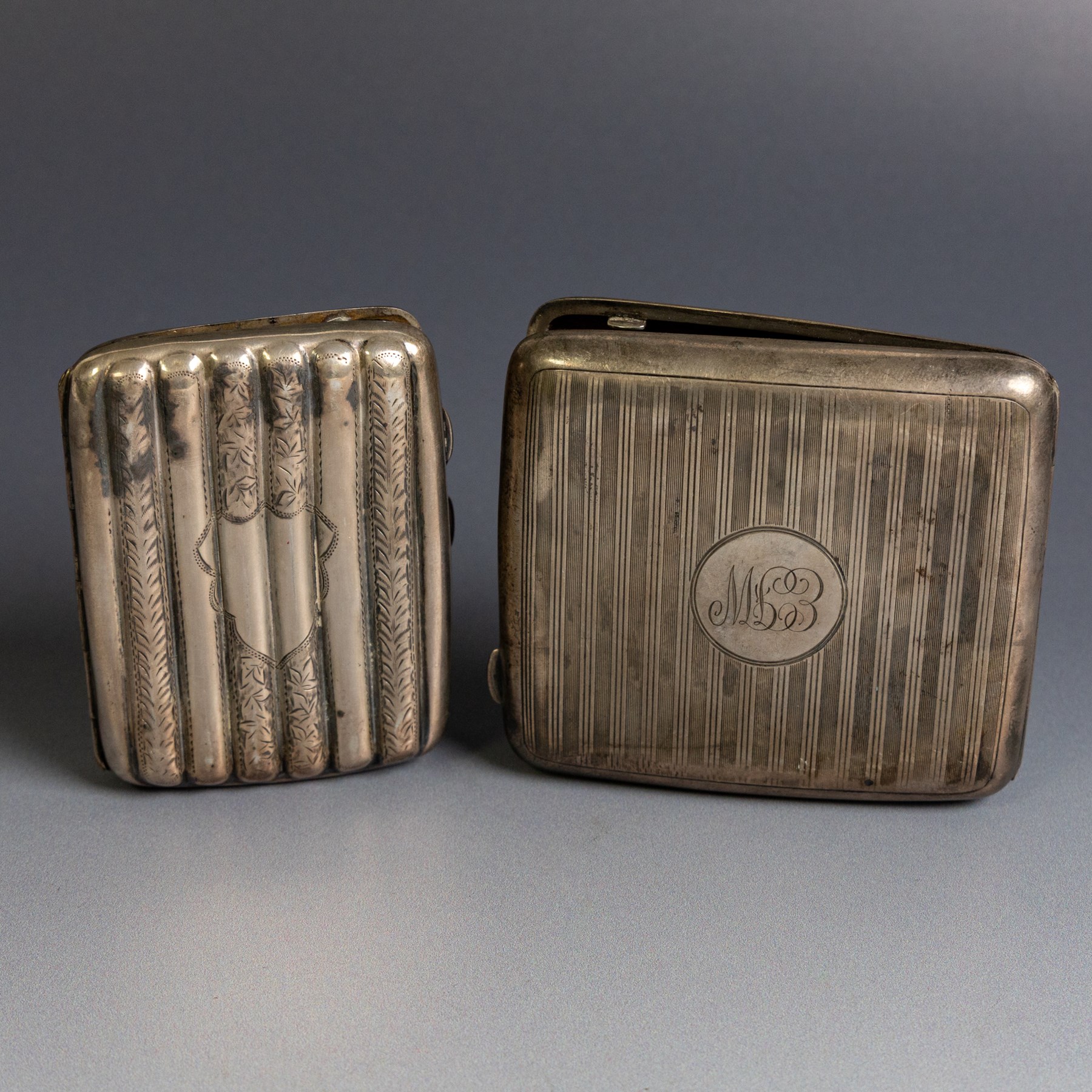 Two early 20th century silver cigarette cases, comprising a rectangular example with foliate decoration and vacant shield cartouche and a 1920s example with engine turned decoration and engraved initials, both hallmarked