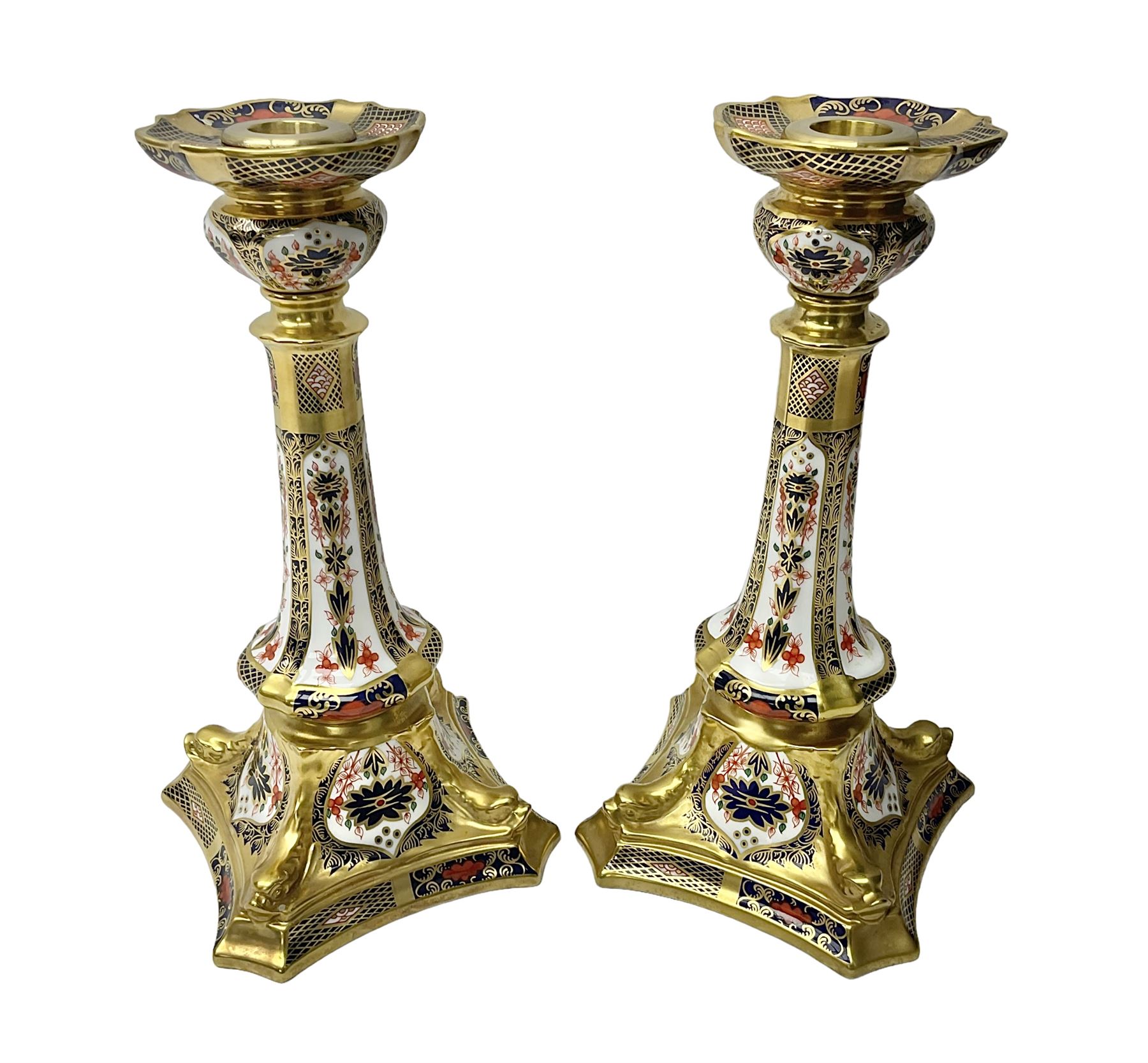 Pair of modern Royal Crown Derby Old Imari 1128 pattern candlesticks, each with shaped drip tray affixed to squat socket, upon spreading stem and canted square base with gilt dolphin edges, with printed marks beneath including Roman numeral year cypher for 2003, H26.5cm, with original boxes