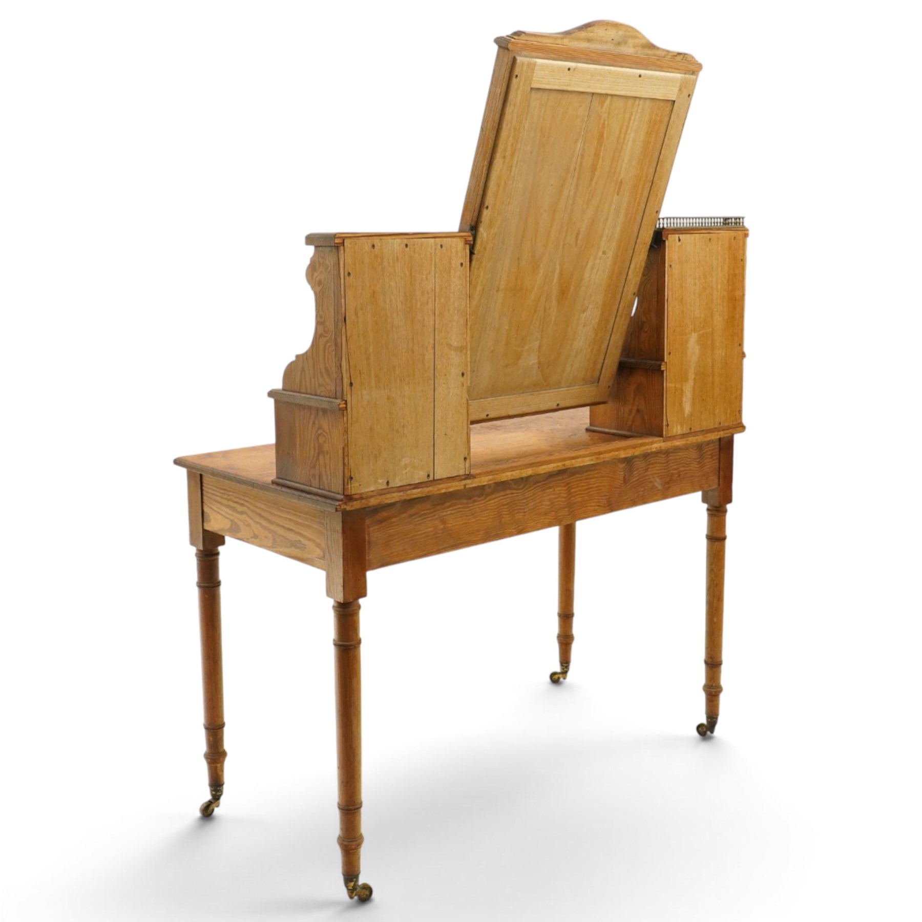 Late Victorian figured pitch pine dressing table, the rectangular swing mirror with shaped cresting flanked by mirrored superstructures, one with a three-quarter galleried shelf, fitted with two drawers, rectangular over two frieze drawers fitted with pierced brass lattice handle plates, raised on ring-turned tapering legs with brass castors
