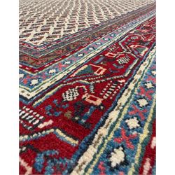 Northwestern Persian Bottehmir hand-knotted rug, ivory field with an all-over design of boteh motifs arranged in diagonal rows within multiple borders and a primary madder red field with stylized vine and flowerhead motifs, 320cm x 214cm 