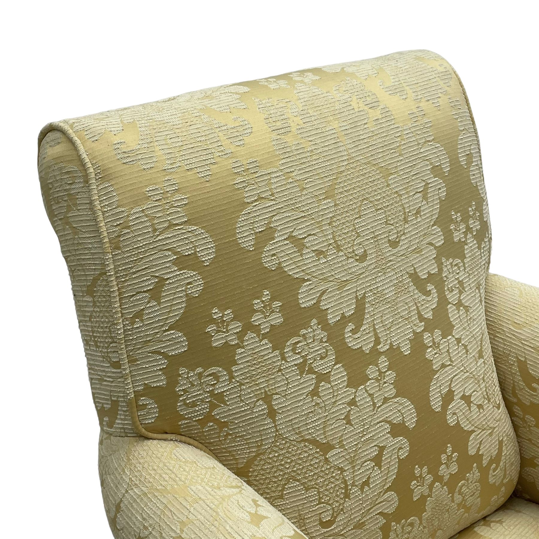 Traditionally shaped hardwood-framed armchair, rolled back and arms, upholstered in pale gold and cream damask fabric with repeating foliate pattern, on turned feet with brass cups and castors