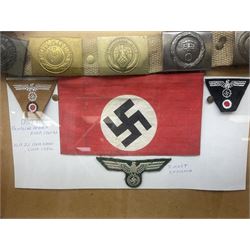 Display of eleven German belt buckles including 'SS', Party Buckle, two Army, Fire Service, two Luftwaffe, NSKK, Hitler Youth and WW1 Army; framed with three cloth badges and an armband