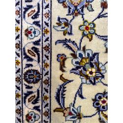 Central Persian Kashan hand-knotted carpet, ivory field with an all-over design of scrolling vines, lotus palmettes, and rosettes in shades of blue, gold, and brown within a blue ground border of palmettes and arabesques between multiple guard stripes