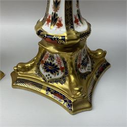 Pair of modern Royal Crown Derby Old Imari 1128 pattern candlesticks, each with shaped drip tray affixed to squat socket, upon spreading stem and canted square base with gilt dolphin edges, with printed marks beneath including Roman numeral year cypher for 2003, H26.5cm, with original boxes