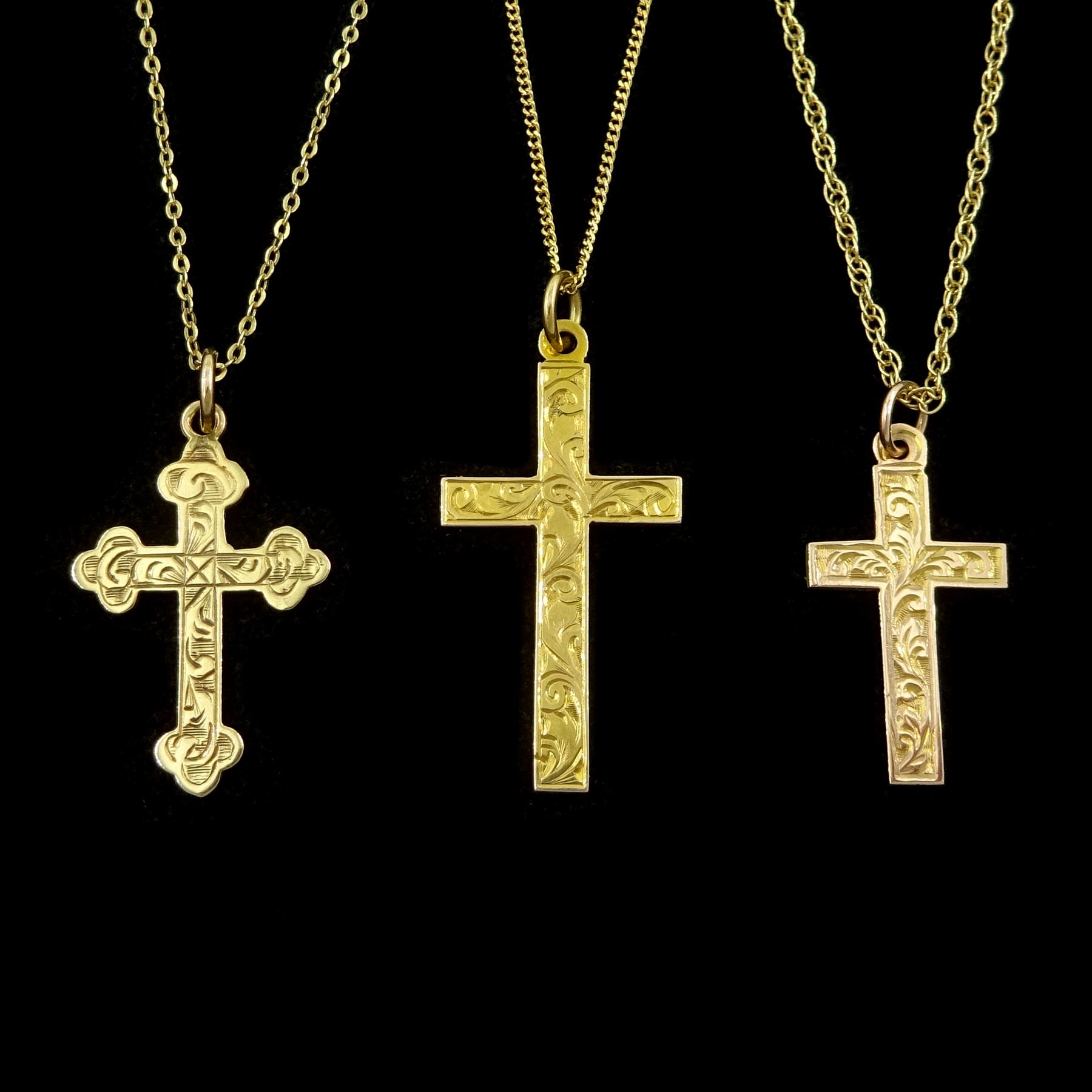 Three early 20th century 9ct gold cross pendants, with engraved decoration, on later 9ct gold chain necklaces