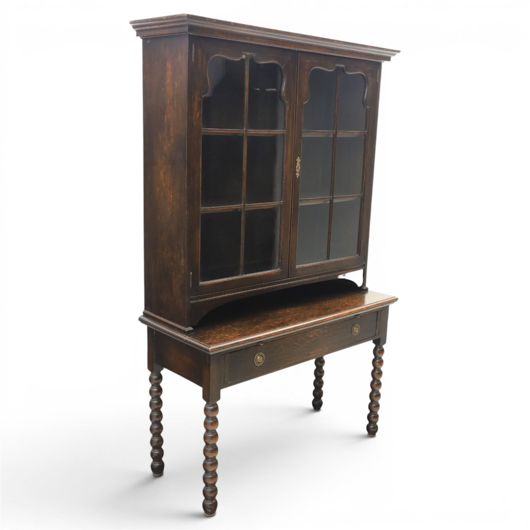 Early 20th century Jacobean Revival dark stained oak dresser, the associated upper section enclosed by twin glazed doors with shaped moulded glazing bars, over separate base fitted with two drawers, raised on bobbin turned legs