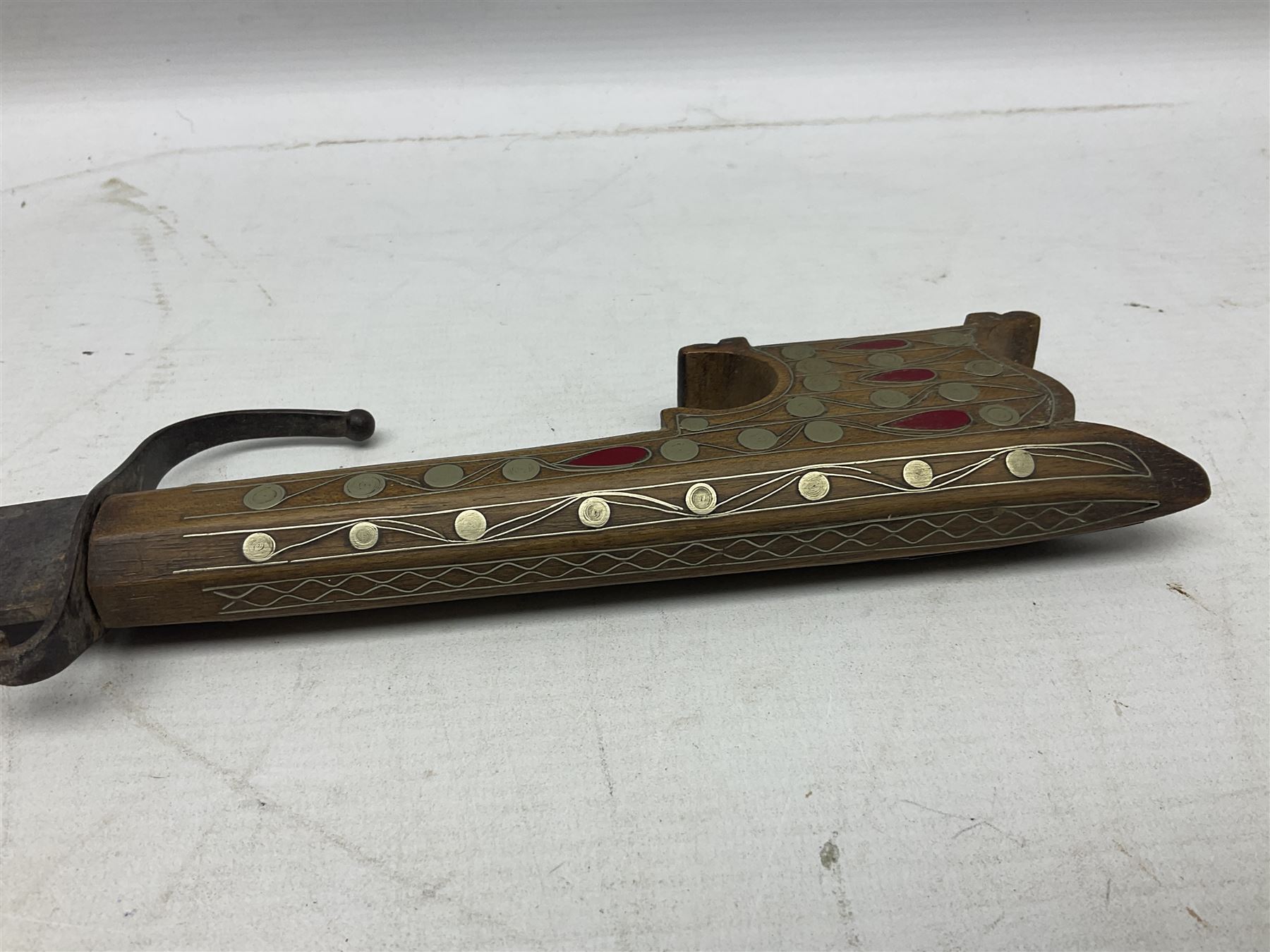 Late 19th/early 20th century Moroccan nimcha dagger-sword, the 40cm curving steel blade with engraved decoration on both sides; shaped hardwood hilt inlaid with brass, white metal wires and red coloured panels; in similarly inlaid scabbard L61cm overall