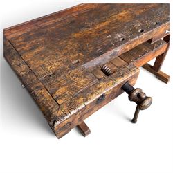 Large early 20th century rustic stained reclaimed pine workbench, the substantial plank top with recessed tool well and two homemade wooden screw vices, above a single frieze drawer and slatted undertier, raised on trestle end supports