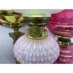 Victorian cast brass oil lamp, with fluted pink glass shade, together with two smaller brass oil lamps with pink shades and reservoirs and a pair of oil lamps, the bases modelled as putti, with pink glass reservoir  and frosted shades, tallest H70cm