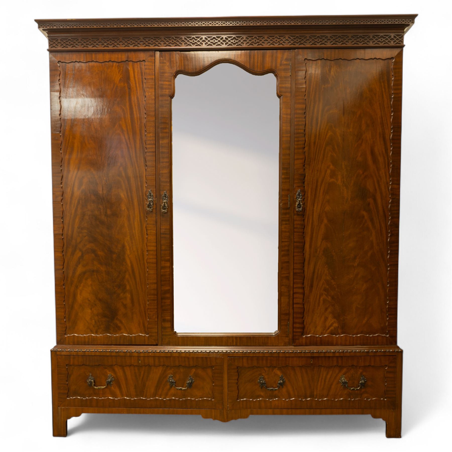 Waring and Gillow - Edwardian style figured mahogany three-section figured wardrobe, moulded and blind fretwork cornice, above three panelled doors, central door with bevelled mirror plate flanked by book-matched flame mahogany panels with moulded borders, above two long drawers with swan-neck handles, raised on bracket feet 