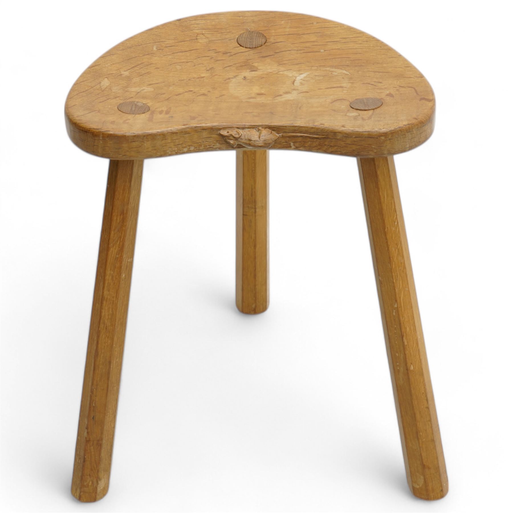 Mouseman - oak three-legged milking stool, dished kidney-shaped seat carved with mouse signature, on three octagonal tapered supports, by the workshop of Robert Thompson, Kilburn