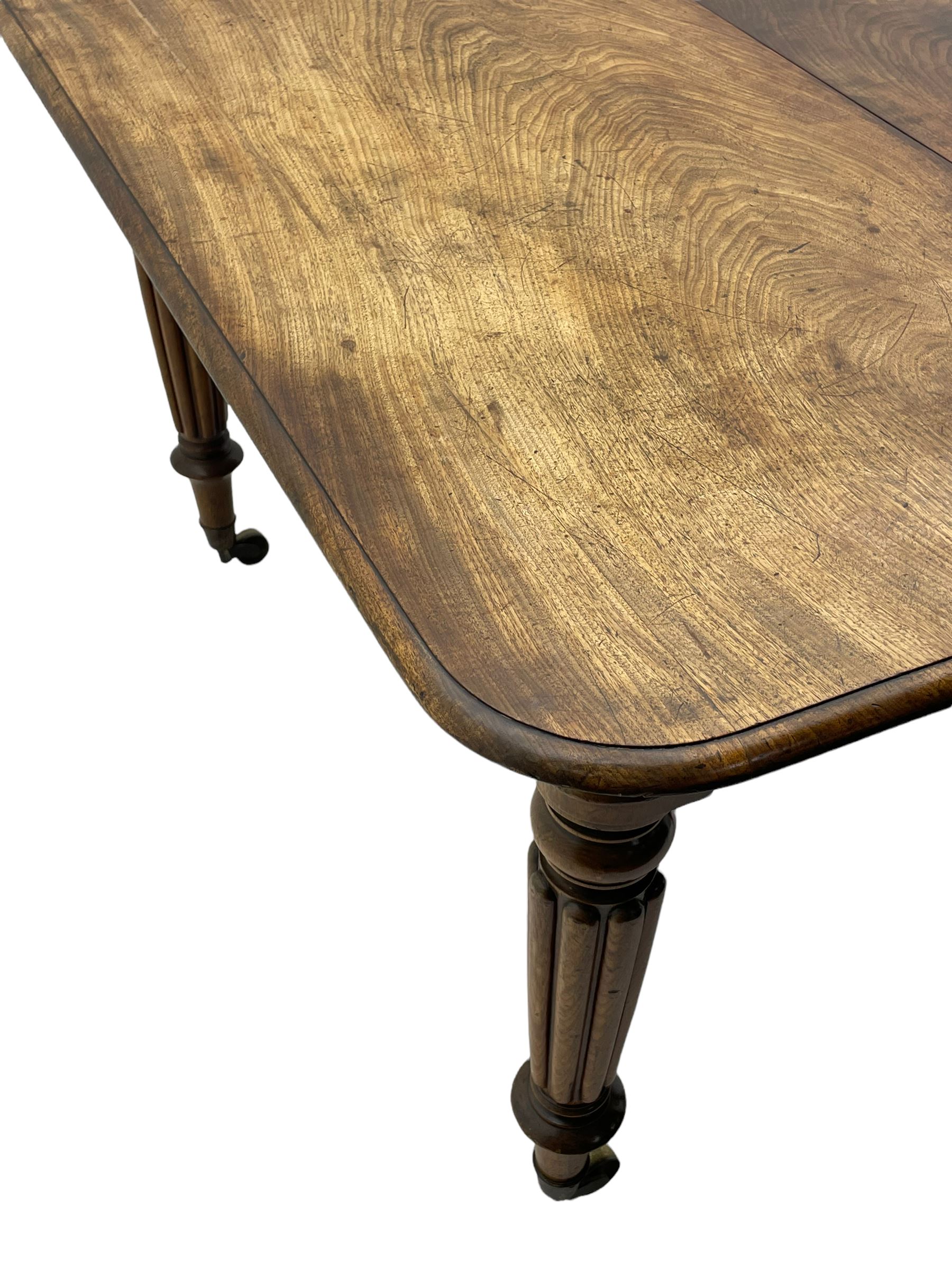 Early 19th century figured mahogany extending dining table, the rectangular top with moulded edge and rounded corners, pull-out action with three additional leaves, raised on turned and lobe carved supports with brass cup castors