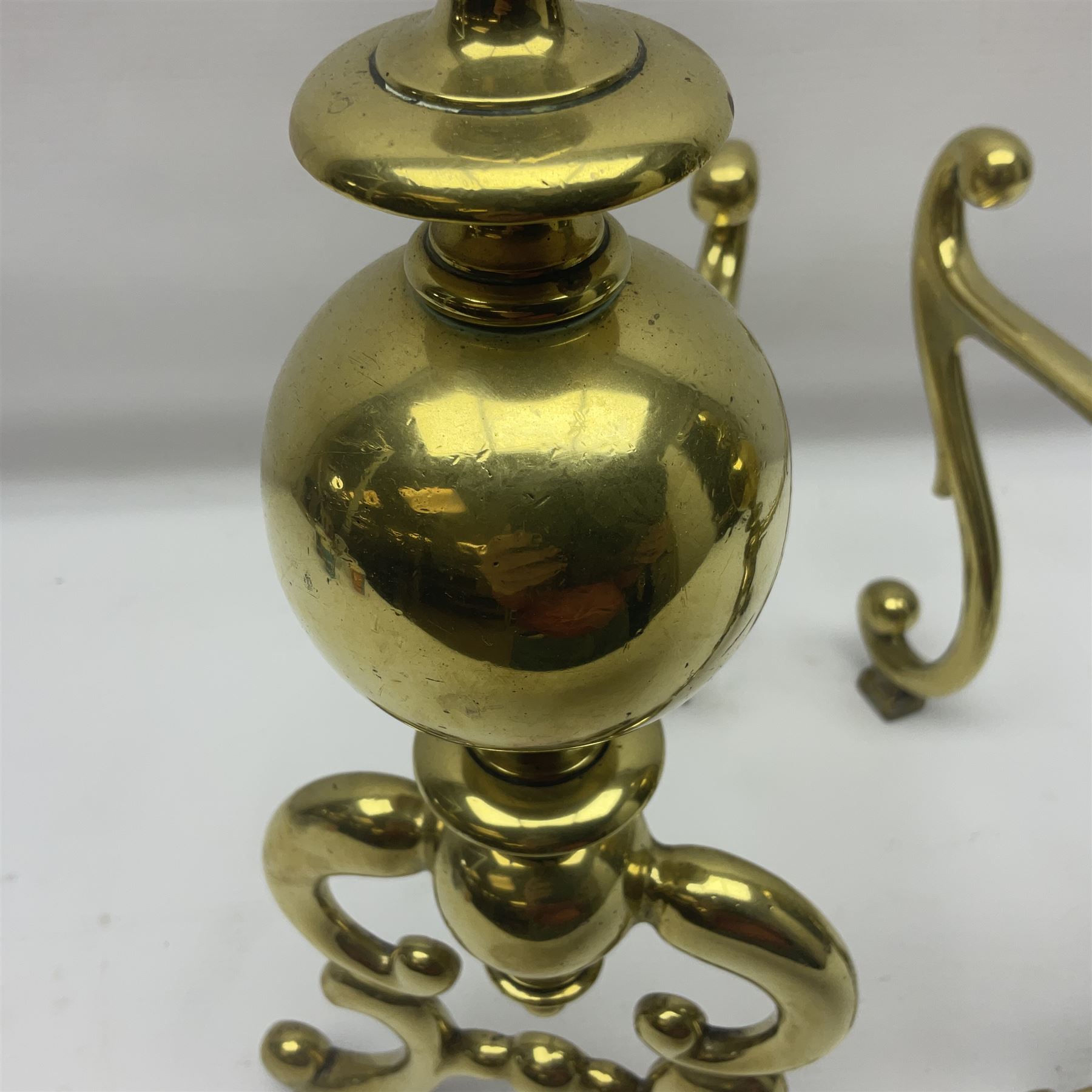 Pair of early 20th century brass fire dogs, each with sphere and urn finial, upon a scrolling base, H38cm