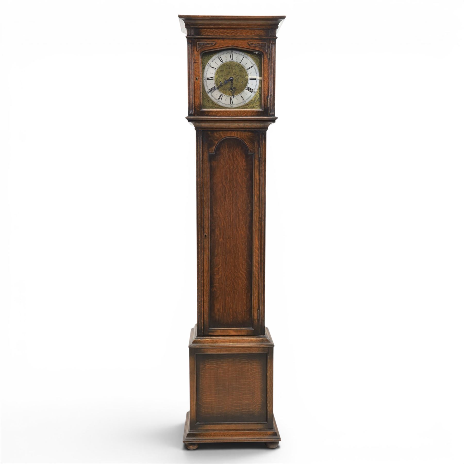 Early 20th century oak longcase clock, square brass dial with engraved foliate spandrels and centre, silvered Roman chapter ring with Arabic minute track, Westminster chime movement, the plain case with glazed arched trunk door and moulded plinth