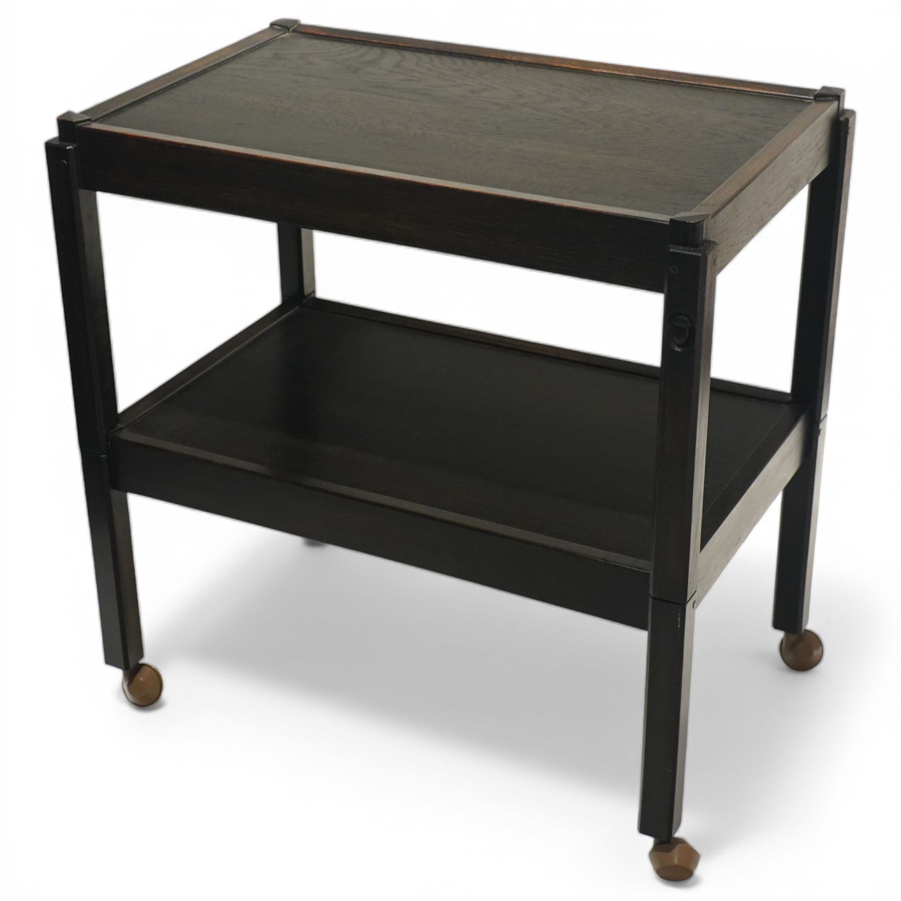 Acornman - dark stained oak two-tier stacking tea trolley, the rectangular removable top, above a second tier raised on castors, with carved acorn signature, by the workshop of Alan Grainger of Brandsby